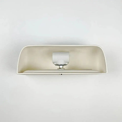 A white, rectangular Gran Balboa Sconce by A19 Artisan Lighting is centered on a plain white wall, viewed from the front. The handcrafted ceramic fixture, made in California, shows the bulb and socket inside.