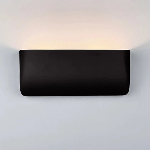 The Gran Balboa Sconce by A19 Artisan Lighting is a handcrafted, USA-made modern black rectangular wall light that emits soft, warm LED light upwards, creating a gentle glow on white walls.