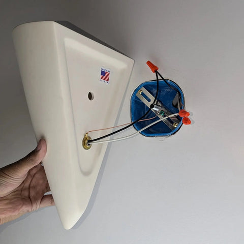 A person prepares to install the Modern USA-Made Wall Lighting – Icelandia Sconce by A19 Artisan Lighting, handcrafted in California, near an electrical box on a gray wall. The sconce features a Made in USA sticker.