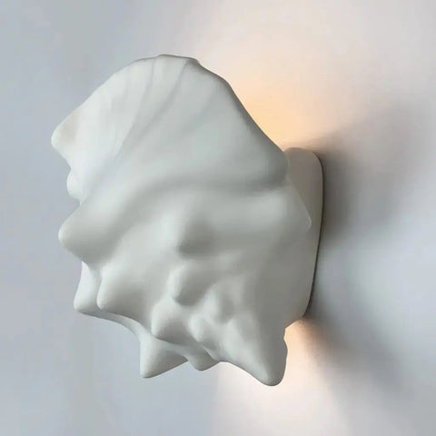 The Modern USA-Made Key West Sconce by A19 Artisan Lighting is a white ceramic seashell-shaped wall fixture, handcrafted in California and LED Smart Bulb compatible, softly glowing against light-colored walls.