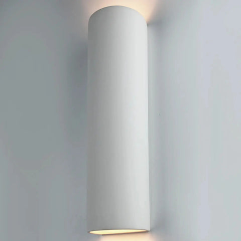 The Kos Sconce by A19 Artisan Lighting is a modern, vertically mounted white wall light handcrafted in California, emitting soft up-and-down light and compatible with LED smart bulbs for customizable ambiance.