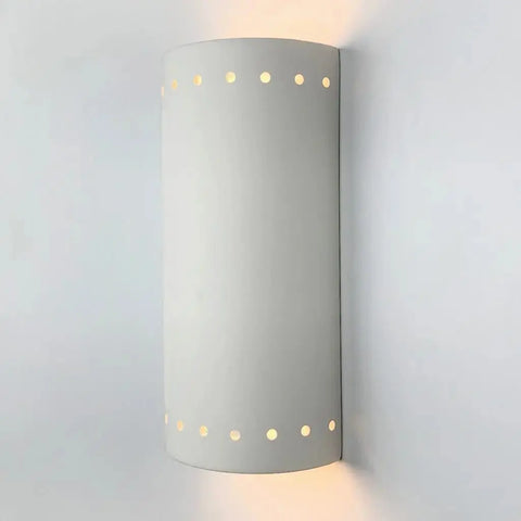 The Kythnos Sconce by A19 Artisan Lighting is a modern, USA-made wall light handcrafted in California. Its matte white cylindrical design with circular cutouts softly emits up and down light, creating a unique ambiance on any wall.