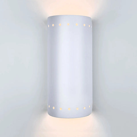 The Modern USA-Made Wall Lighting – Kythnos Sconce by A19 Artisan Lighting is a handcrafted, white cylindrical wall light with small holes near the top and bottom, casting soft up-and-down light against a light gray wall.