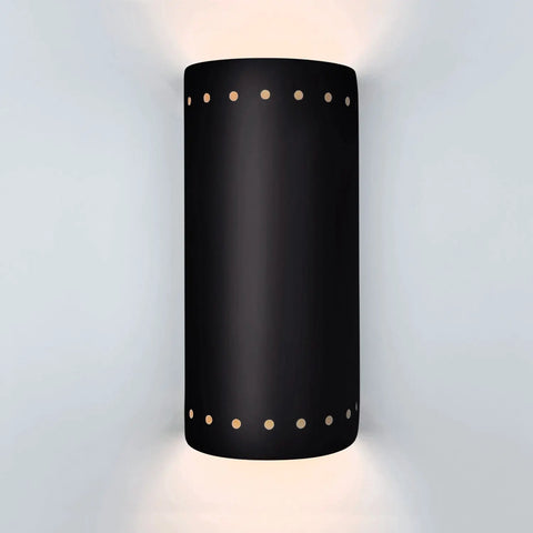 The Kythnos Sconce by A19 Artisan Lighting is a USA-made black cylindrical wall light, handcrafted in California, with small circular cutouts near the top and bottom that cast up and down light on white walls.