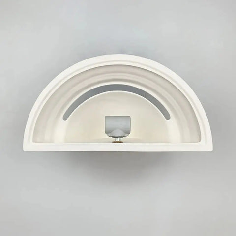Overhead view of a modern, semi-circular white sink with a minimalist metal faucet and drain, set against a light gray background accented by the Modern USA-Made Majorca Sconce from A19 Artisan Lighting, handcrafted in California.