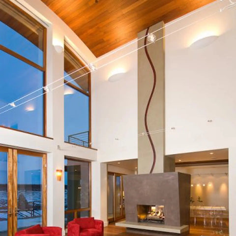 Modern living room with high ceilings, floor-to-ceiling windows, a contemporary fireplace, and red armchairs. Handcrafted Maui Sconces by A19 Artisan Lighting add stylish illumination and highlight the outdoor views.