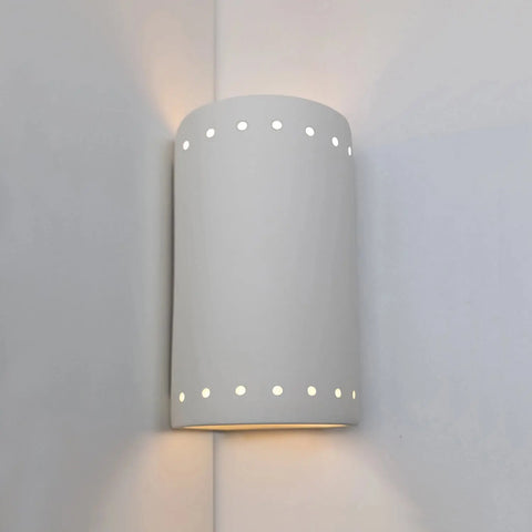 The Modern USA-Made Melos Corner Sconce by A19 Artisan Lighting is handcrafted in California, featuring perforated ceramic with rows of small circular holes to cast soft light where two white walls meet.