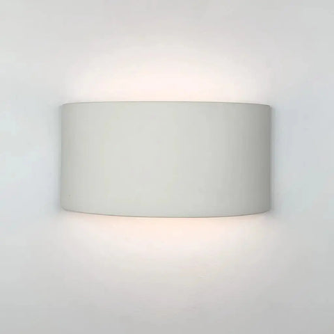 A shield-shaped, white ceramic flush wall light fixture, showing an up-and-down light pattern.