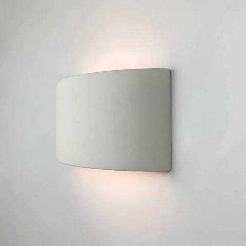 The Modern USA-Made Wall Lighting – Nicosia Sconce by A19 Artisan Lighting features a smooth, curved rectangular design, handcrafted in California, and casts a soft, warm glow both upward and downward on any plain white wall.