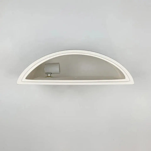 A white, half-circle Nicosia Sconce from A19 Artisan Lighting, handcrafted in California, features a small cylindrical lamp and is mounted on a plain light gray wall.