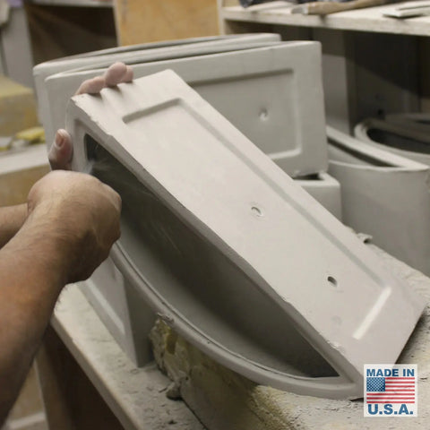 In a workshop, someone smooths the edge of a rectangular ceramic piece from the Modern USA-Made Wall Lighting – Nicosia Sconce by A19 Artisan Lighting. Stacked pieces, an American flag, and a handmade in the USA label are also visible.