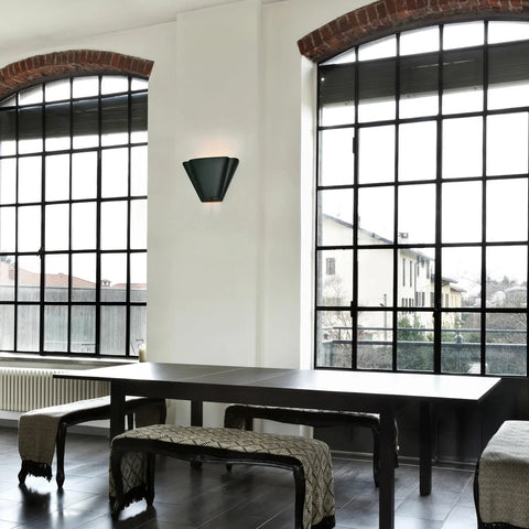 A modern dining area with a black table, benches, large arched windows, and a Modern USA-Made Wall Lighting – Nova Scotia Sconce by A19 Artisan Lighting, handcrafted in California, letting in natural light and views of buildings and trees outside.