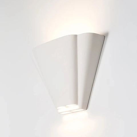 The Modern USA-Made Nova Scotia Sconce by A19 Artisan Lighting, handcrafted in California, features a fan-shaped design that casts soft up and down light against a white wall, blending artisan quality with contemporary style.