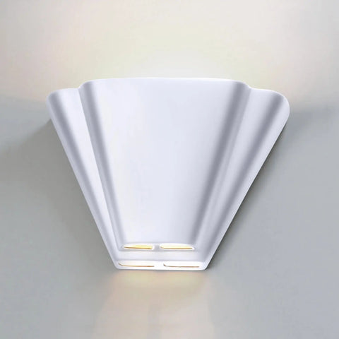 The Modern USA-Made Nova Scotia Sconce by A19 Artisan Lighting features a fan-shaped, handcrafted white design with soft uplighting and subtle bottom cutouts emitting a warm glow, mounted on a light gray wall for contemporary appeal.