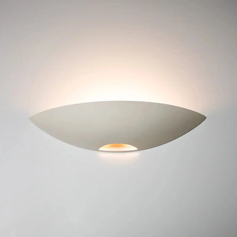 The Modern USA-Made Wall Lighting – Oahu Sconce by A19 Artisan Lighting features a curved white shade that softly uplights plain walls, creating a gentle glow above this handcrafted California fixture.