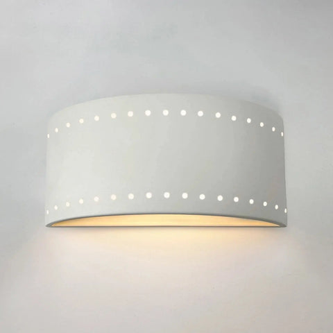 The Paros Downlight Sconce by A19 Artisan Lighting is a modern, handcrafted white wall fixture featuring rows of circular cutouts, made in California, and casting warm light downward onto the wall.