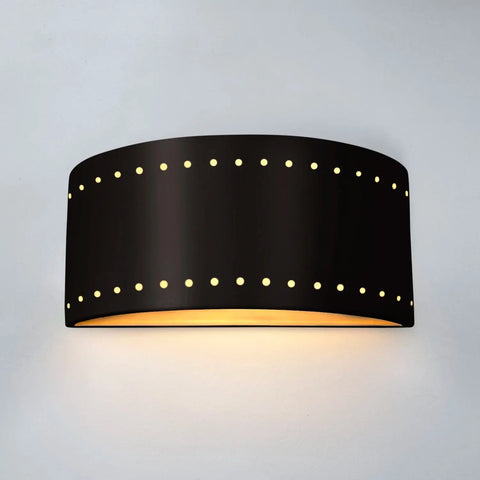 The Paros Downlight Sconce by A19 Artisan Lighting is a modern, USA-made black wall fixture with a curved rectangular shape and perforated rows for LED light, shown mounted on a light-colored wall. Handcrafted in California.