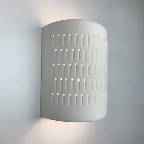 The Modern USA-Made Samos Sconce by A19 Artisan Lighting is a handcrafted white ceramic wall light with a rounded, perforated design, emitting soft, diffused light. Compatible with LED bulbs for sustainable lighting. Made in California.