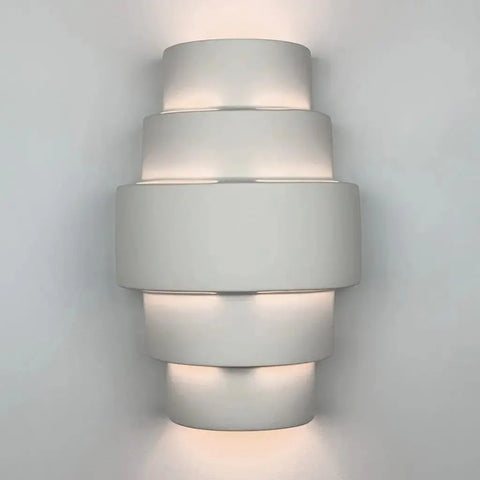 The San Marcos Sconce by A19 Artisan Lighting is a handcrafted, modern wall light made in California. Its customizable finish casts soft up-and-down light, adding a geometric, layered touch to any white wall.