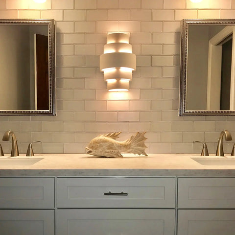 Modern bathroom vanity with dual sinks, a decorative fish sculpture, and an energy-efficient A19 Artisan Lighting San Marcos Sconce—handcrafted in California—centered between two mirrors against a tiled backsplash.