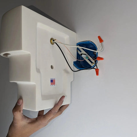 A hand holds the Santa Cruz Sconce—Modern USA-Made Wall Lighting by A19 Artisan Lighting, handcrafted in California, with exposed wires to an electrical box and a Made in USA sticker. Ideal for energy-efficient LED smart bulbs.