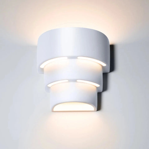 The Santa Cruz Sconce by A19 Artisan Lighting is a modern, USA-made wall light handcrafted in California, featuring a white layered cylindrical design and soft LED illumination for a stylish glow.