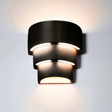 The Santa Cruz Sconce by A19 Artisan Lighting is a modern, black, tiered wall light handcrafted in California with energy-efficient LED bulbs casting layered white light up and down on your wall.