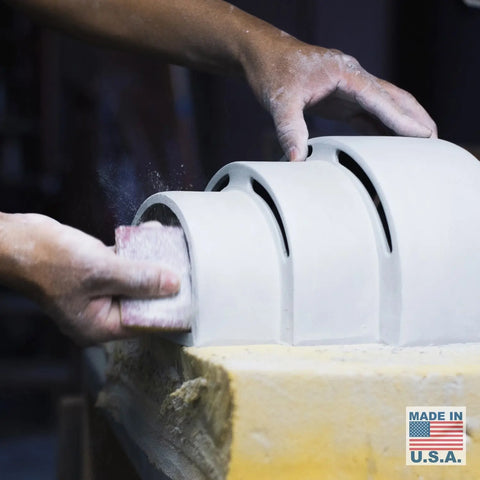 Hands sanding a curved ceramic piece with white dust, beside a Made in U.S.A. label and flag—showcasing A19 Artisan Lighting’s Modern USA-Made Wall Lighting: Santa Cruz Sconce, handcrafted in California and ideal for LED smart bulbs.