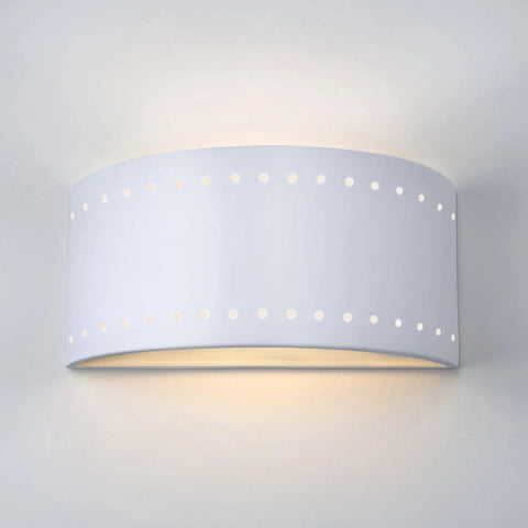 The Modern USA-Made Wall Lighting – Syros Sconce by A19 Artisan Lighting is handcrafted in California, featuring a curved ceramic design with two rows of circular holes that emit a soft glow for a contemporary look.