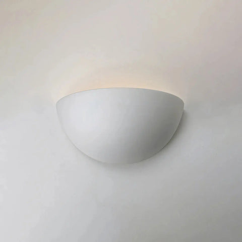 The Thera Sconce by A19 Artisan Lighting is a handcrafted, USA-made flush wall light with a sleek semi-circular design. Mounted on a light wall, it casts an upward glow and offers customizable finishes for any modern space.