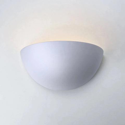 The Thera Sconce by A19 Artisan Lighting is a handcrafted, white half-sphere wall light made in California. Its customizable finish blends seamlessly into modern spaces, casting a soft upward glow on any plain white wall.