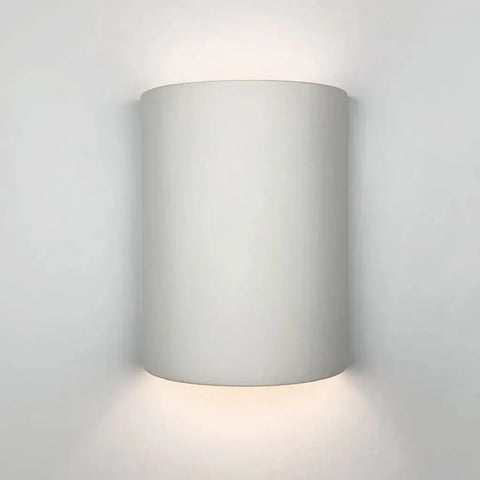 The Modern USA-Made Tilos Sconce by A19 Artisan Lighting, handcrafted in California, is mounted on a white wall and casts gentle up-and-down light.
