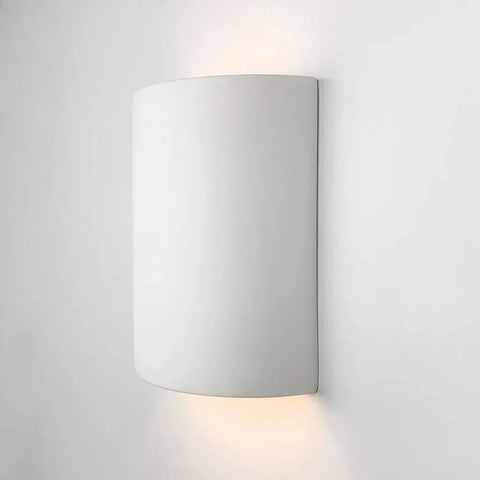 The Modern USA-Made Tilos Sconce by A19 Artisan Lighting is a handcrafted, curved white fixture emitting soft light from top and bottom, shown mounted on a plain wall. Part of the Islands of Light Collection, made in California.