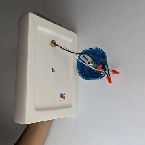 A hand holds a white rectangular Tilos Sconce from A19 Artisan Lighting near a walls blue electrical box with wires connected by wire nuts. This Modern USA-Made Wall Lighting is handcrafted in California and features a Made in USA sticker.