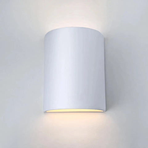 The Modern USA-Made Tilos Sconce by A19 Artisan Lighting, handcrafted in California, emits soft up and down lighting against a plain white wall.