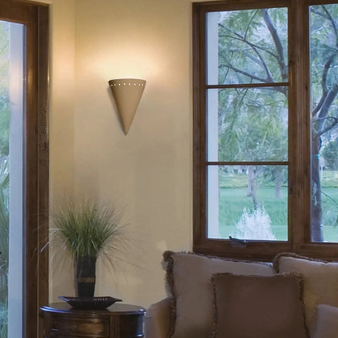 The Modern USA-Made Zealandia Downlight Sconce by A19 Artisan Lighting, handcrafted in California, emits warm light in a cozy living room with beige walls, a cushioned sofa, greenery, and windows overlooking trees and grass.