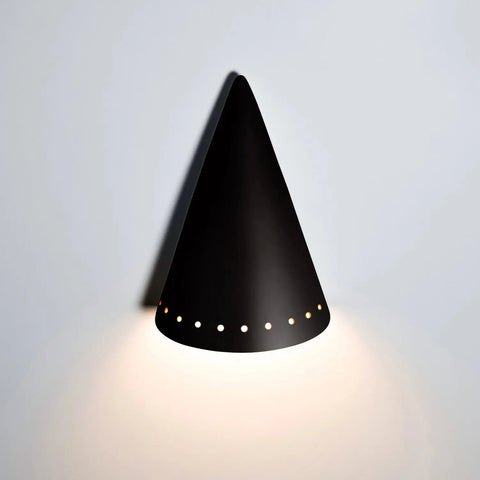 The Zealandia Downlight Sconce by A19 Artisan Lighting is a handcrafted, black, cone-shaped ceramic wall light made in California, with small round holes near the base casting soft downward light on a white wall.
