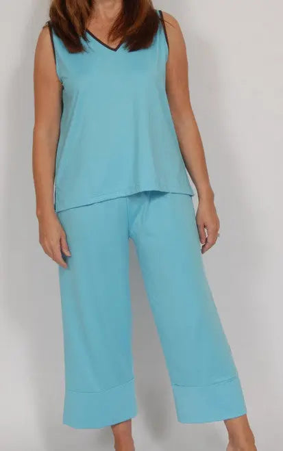 A woman, face unseen, stands against a plain background wearing the Goodnighties Cropped Pant and matching sleeveless, loose-fitting light blue top made from anti-microbial fabric.