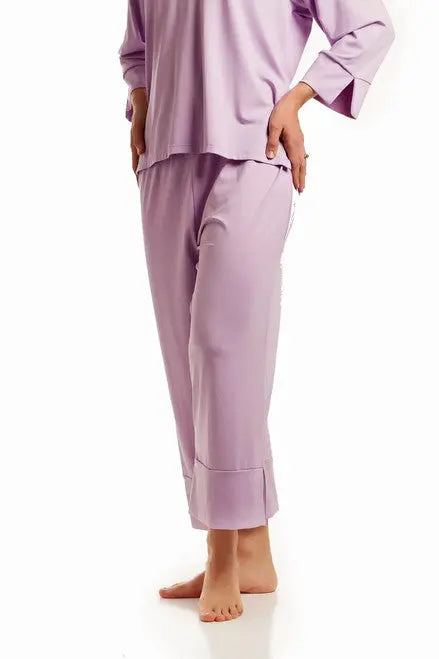 A person stands barefoot in a loose-fitting, long-sleeved lavender Goodnighties pajama set with anti-microbial fabric and Cropped Pant, shown against a white background. The head is not visible.