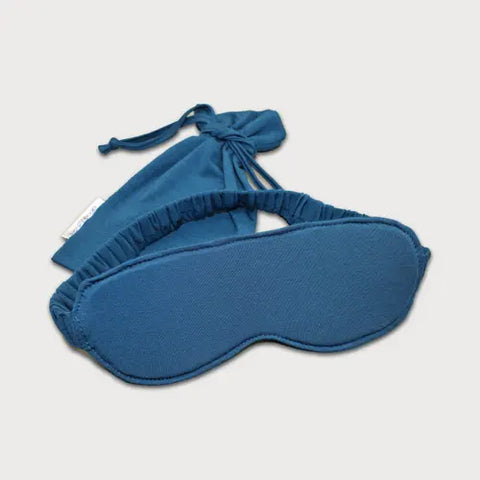 The Goodnighties Sleep Mask With Pouch features a handcrafted mask with an elastic band, placed in front of its matching blue drawstring pouch on a plain white background.