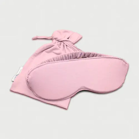 The Goodnighties Sleep Mask With Pouch features a light pink, handcrafted mask with an elastic band and a matching drawstring pouch, displayed against a plain light background.