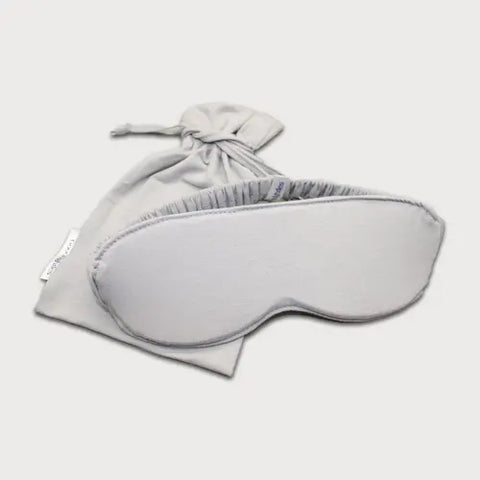 The Goodnighties Sleep Mask With Pouch, in light gray, features moisture-wicking fabric and an elastic band, shown alongside its matching drawstring pouch on a white background.