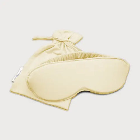 The Goodnighties Sleep Mask With Pouch features a pale yellow, handcrafted mask with soft ruffled edges and a matching drawstring pouch, both made from smooth fabric, displayed on a plain white background.