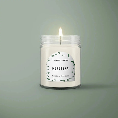 The Monstera - Signature Candle by Sawdust & Embers comes in a clear glass jar with green leaf designs and a fresh scent, bringing stylish fragrance to any room.