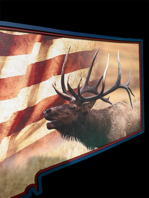 A bull elk with large antlers stands before a faded American flag, all within the Montana shape on black—a striking piece from B. James Design & Woodwork's Montana Elk Flag Sign, perfect for fans of Montana craftsmanship.