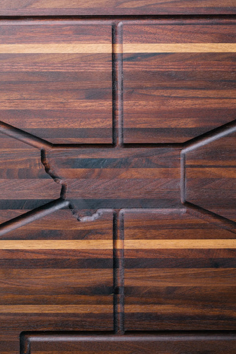 The Montana Carver - Walnut by Montana Block is an edge grain walnut cutting board with grooves outlining Montana at the center, framed by rectangular and linear patterns in contrasting wood tones for lasting durability.