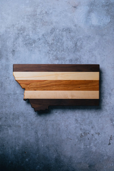 The Montana by Montana Block features handcrafted light and dark wood stripes on a textured gray surface, making it an ideal personalized kitchen gift.