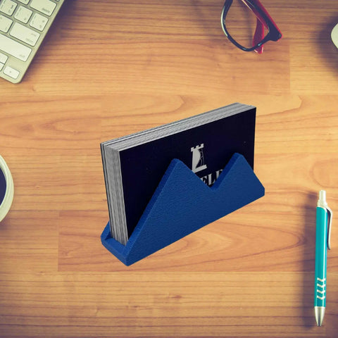 A stack of business cards sits in the Chatelet Manufacturing Mountain Silhouette Design Business Card Holder Display on a wooden desk near a keyboard, red glasses, a pen, and a coffee cup.