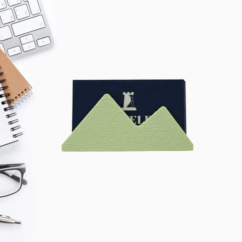 The Mountain Silhouette Design Business Card Holder Display by Chatelet Manufacturing stylishly displays business cards with a chic green mountain design, shown on a white desk beside office essentials for a perfect workspace accessory.