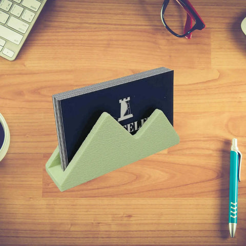 The Chatelet Manufacturing Mountain Silhouette Design Business Card Holder stylishly displays black business cards on a wooden desk, adding charm among a keyboard, red glasses, pen, and a steaming cup of coffee.